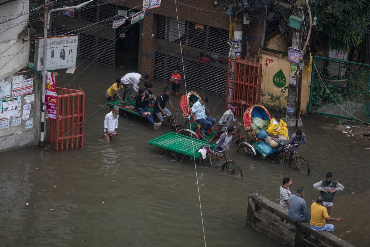 People with rickshaws struggle through knee-deep water in a street following heavy rains.
