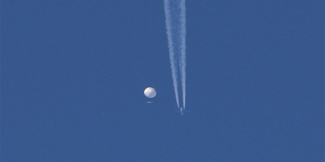 A large balloon drifts above the Kingston, North Carolina area, with an airplane and its contrail seen below it. 