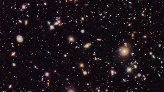 A spray of galaxies and stars looking small against the darkness of space.