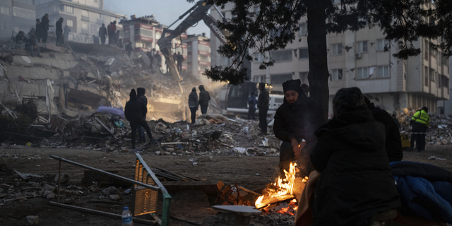 People warm around a fire as rescuers search in a destroyed building in Kahramanmaras, southeastern Turkey, on Thursday, Feb. 9.