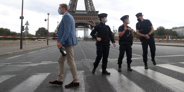 A Russian tourist walks past police officers at the bridge leading to the Eiffel Tower, Sept. 23, 2020, in Paris.