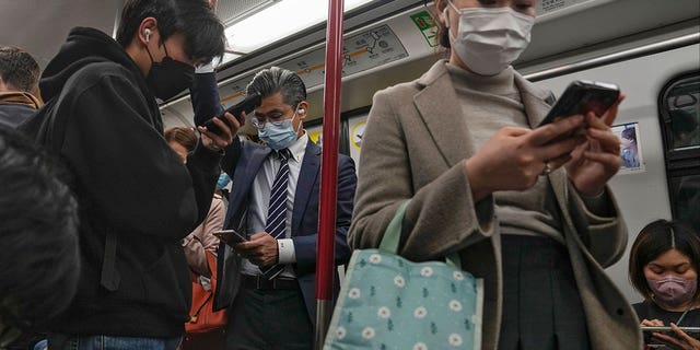 Commuters wearing face masks browse their smartphones as they ride on a subway train in Hong Kong on Feb. 7, 2023. Hong Kong will lift its mask mandate Wednesday.