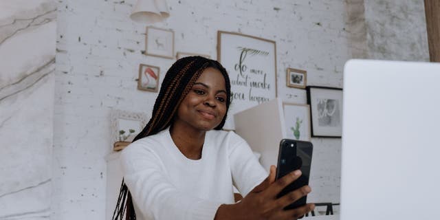 A woman gives a soft smile while looking at her iPhone, as she holds it out in front of her. 