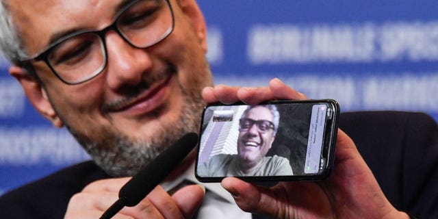 Iranian producer Farzad Pak holds a phone displaying Iranian director Mohammad Rasoulof who was awarded the "Golden Bear for Best Film" for his film "There is No Evil."