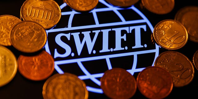 SWIFT (Society for Worldwide Interbank Financial Telecommunication) logo displayed on a phone screen and coins are seen in this illustration photo taken in Krakow, Poland on January 23, 2022.