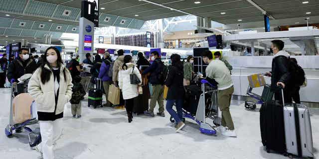 Travelers stand in line near check-in counters in a departure hall at Narita International Airport in Narita, Japan, on Dec. 30, 2022. Japan is easing COVID-19 border measures for tourists from China. 