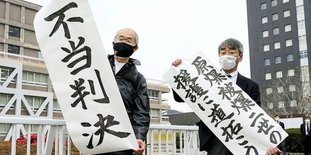 Plaintiff Katsuhiro Hirano, right, and an unidentified lawyer for the plaintiffs display signs in Hiroshima, Japan, on Feb. 7, 2023. The banners read "Pave the way to backup Second-Generation Atomic Bomb Survivors," right, and "Unfair judgement."