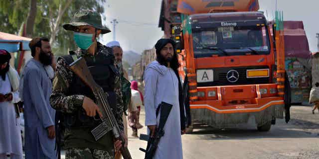 A Pakistani paramilitary soldier, front, and Taliban fighters stand guard on their respective sides of the Afghan-Pakistan border while a truck moves at a crossing point in Torkham, in Khyber district, Pakistan.