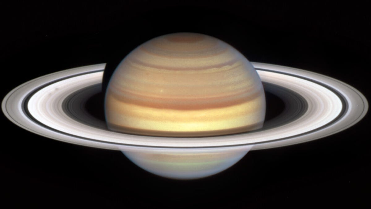 Saturn looks like a swirled beige, pink and yellow marble with light rings around it with some dark streaks and shadowy formations like little blotches (known as spokes).