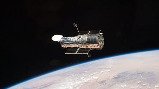 Hubble looks like a shiny cylinder against the dark of space with the curve of Earth below.