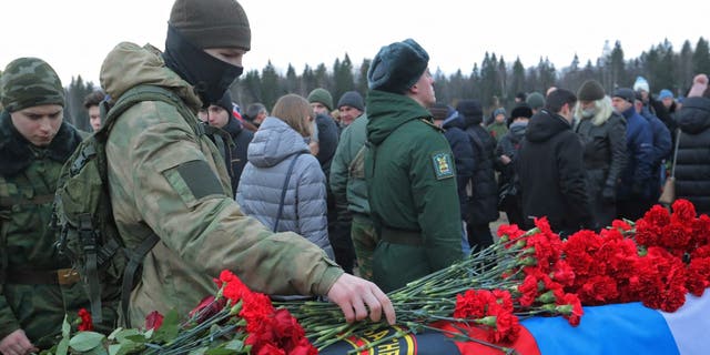 A man places flowers at the coffin during the funeral of Dmitry Menshikov at a cemetery in Saint Petersburg, Russia, Dec. 24, 2022. Menshikov was a mercenary for the private Russian military company Wagner Group who was killed during the military conflict in Ukraine.