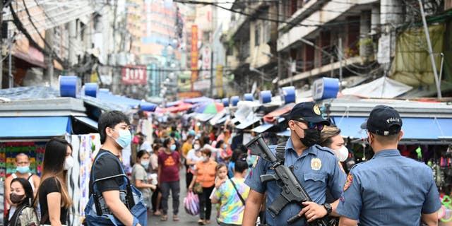 A policeman carrying an automatic rifle stands guard with a colleague along a popular market street in Manila, Philippines, on June 1, 2022.