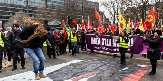 A protester prepares to jump on a banner with the image of Turkish President Recep Tayyip Erdogan during a demonstration in Stockholm on Jan. 21, 2023. (Christine Olsson/TT News Agency via AP)