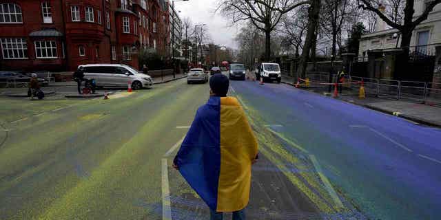 A protester wears an Ukraine flag after a group painted a giant Ukrainian flag outside the Russian Embassy in London on Feb. 23, 2023. 