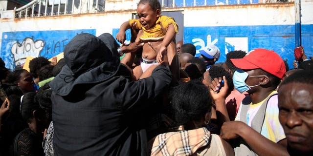 A parent tries to hand off his daughter to get her through the gate of Haiti´s immigration office as they wait their turn to apply for a passport, in Port-au-Prince, Haiti, Thursday, Feb. 9, 2023. 