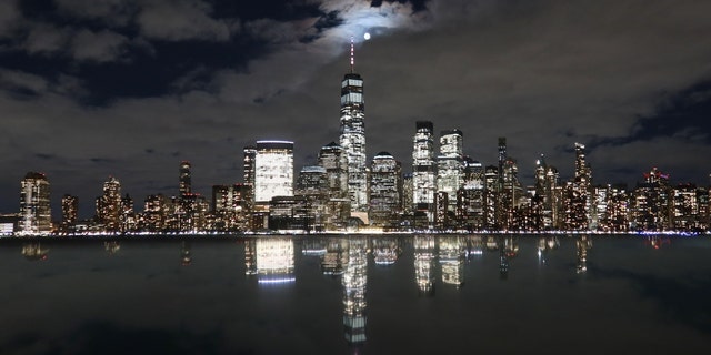 The full Worm Moon rises on a cloudy evening behind the skyline of lower Manhattan and One World Trade Center in New York City as it is reflected in the top of a monument on March 7, 2023, as seen from Jersey City, New Jersey. 