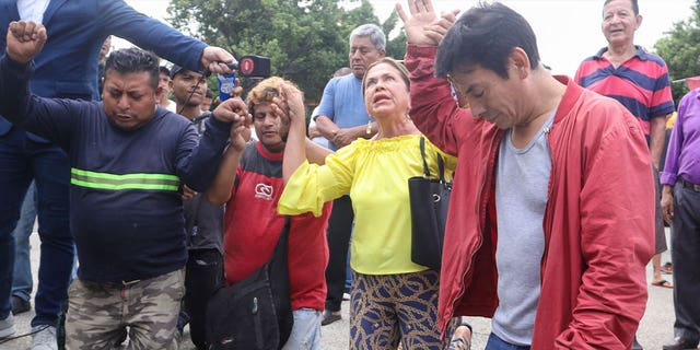 Residents pray as police officers aid a security guard who had explosives taped to his torso in Guayaquil, Ecuador, on March 30, 2023. 