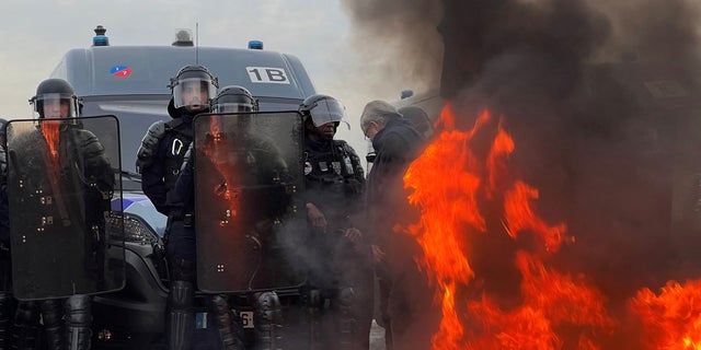 French gendarmes and CRS riot police stand on position near a fire as demonstrators gather on Place de la Concorde near the National Assembly in Paris, France, March 16, 2023. 