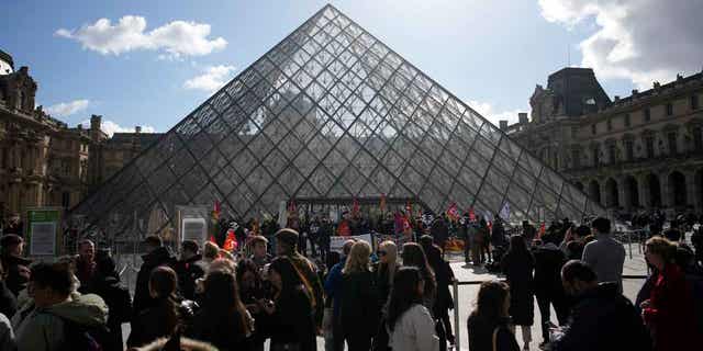 Visitors wait as demonstrators protest outside the Louvre Museum on March 27, 2023, in Paris. President Emmanuel Macron inflamed public anger by sending his already unpopular plan to raise the retirement age by two years through parliament without a vote. 
