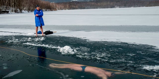 A man stands next to the Barbora Lake near Teplice city where his friend, Czech free diver David Vencl, swims under ice in the Czech Republic on Feb. 13, 2021.