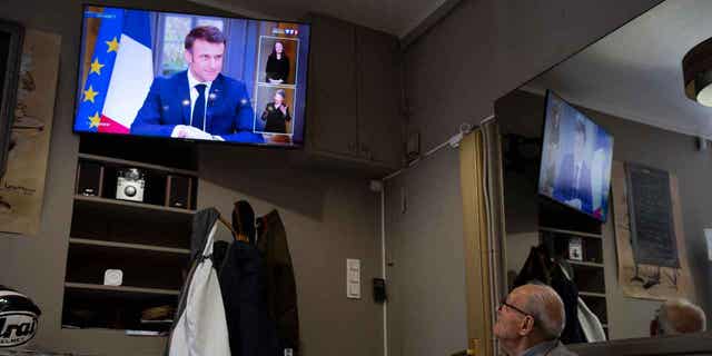 A man watches French President Emmanuel Macron speak during an interview with journalists on television in Marseille, France, on March 22, 2023. Macron said the controversial pension bill should be implemented by the "end of the year." 