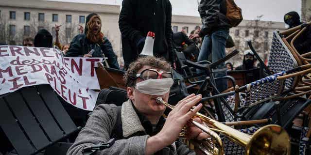 A man plays the trumpet in front of a barricade during a demonstration in Lyon, France, on March 7, 2023. 