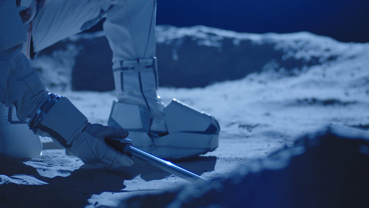 A scientist in a spacesuit's boots seen on what looks like lunar soil.
