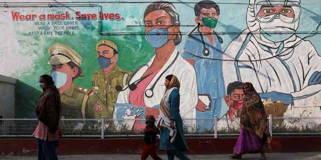 Women walk past graffiti amidst the spread of the coronavirus disease in New Dehli, India. The capital city is ramping up testing for the virus after an increase in cases.