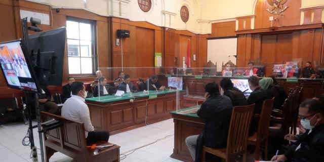 Police officer Hasdarmawan, left, sits on the defendant's chair during his sentencing hearing at a district court in Surabaya, Indonesia, on March 16, 2023. The Indonesian court sentenced Hasdarmawan to 18 months in prison for negligence leading to the deaths of 135 people in October. Other officers who played less of a role in the incident were acquitted in court.