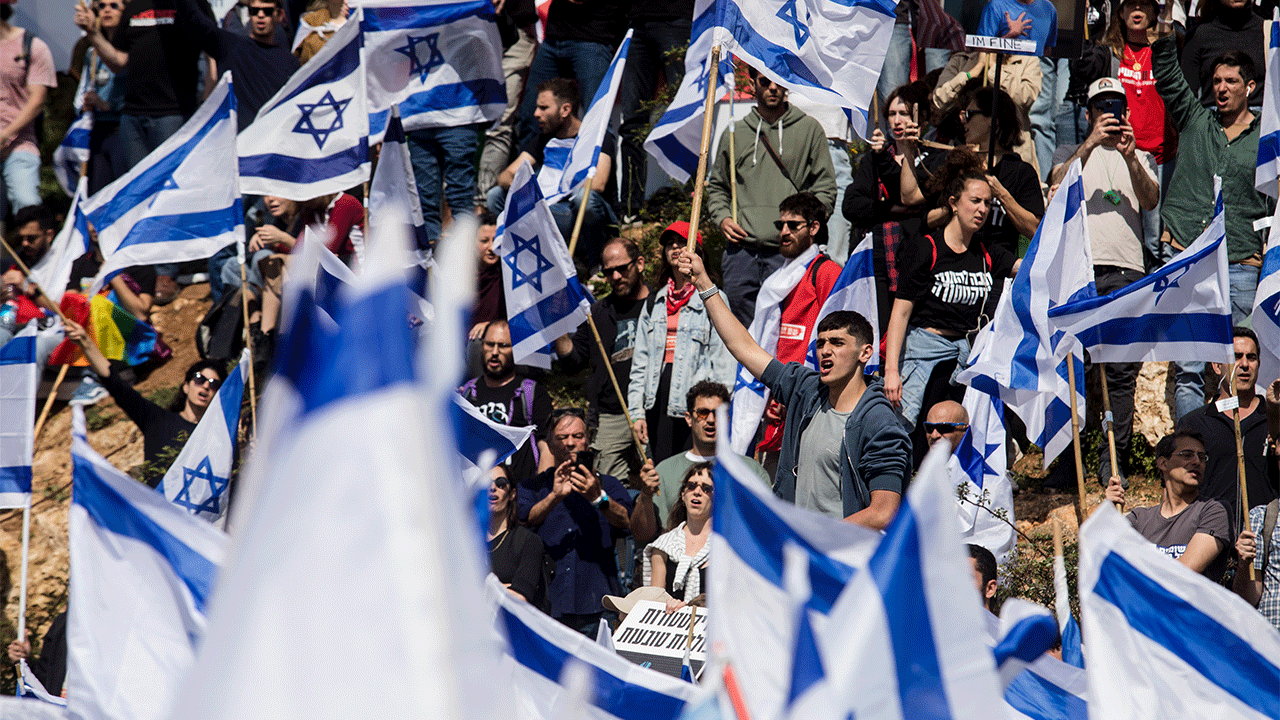 Protestors wave flags as thousands of Israelis attend a rally against Israeli Government's judicial overhaul plan on March 27, 2023 in Jerusalem. Yesterday's dismissal of Defense Minister Yoav Gallant intensified the political crisis sparked by the Netanyahu government's planned judicial overhaul, designed to limit the court's authority over Parliament.