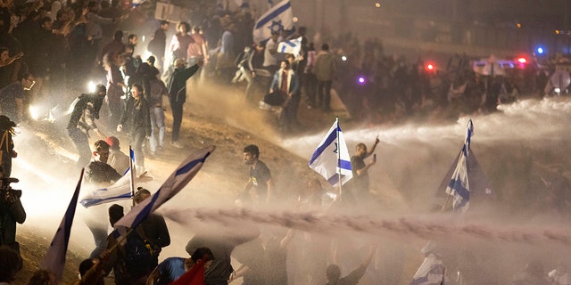 Israeli police use a water cannon to disperse demonstrators blocking a highway during a protest against plans by Prime Minister Benjamin Netanyahu's government to overhaul the judicial system in Tel Aviv, Israel, Monday, March 27, 2023.