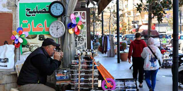 A Lebanese street vendor who also sells and repairs clocks, sits next to two clocks that show different times in Lebanon, on March 27, 2023. Lebanon's caretaker prime minister reversed a decision to delay the start of daylight saving time by a month.