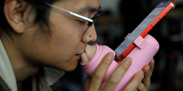 Jing Zhiyuan uses a remote kissing device "Long Lost Touch," as he demonstrates for camera how to use it during an interview with Reuters, at his home in Beijing March 12, 2023.