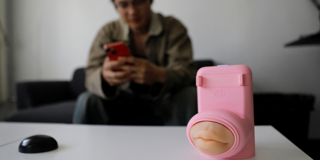 Jing Zhiyuan uses his phone near a remote kissing device "Long Lost Touch," as he demonstrates how to use it during an interview with Reuters, at his home in Beijing March 12, 2023.