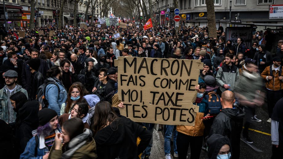 A protester holds a banner reading 'Macron do what I do, tax your friends'
