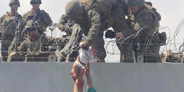 A U.S. Marine grabs an infant over a fence topped with concertina wire during the evacuation at Hamid Karzai International Airport in Kabul on Aug. 19, 2021.