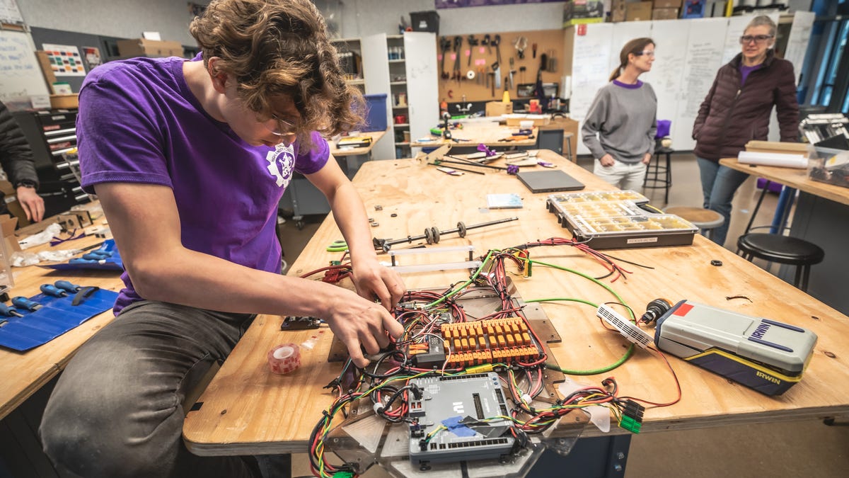 A student in a purple T-shirt works on a circuit board for a robot