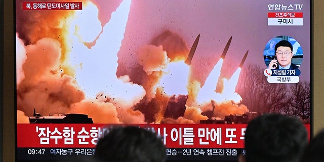 People stand near a television showing a news broadcast with file footage of a North Korean missile test, at a railway station in Seoul on March 14, 2023.