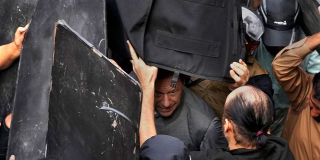 Security personnel hold bulletproof shields to secure former Prime Minister Imran Khan, center, after appearing in a court, in Lahore, Pakistan, on March 21, 2023.