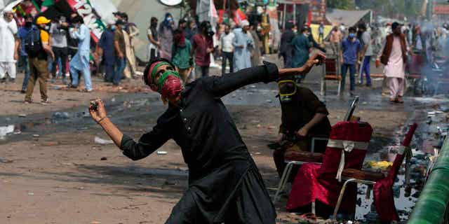 A supporter of former Prime Minister Imran Khan throws a stone towards riot police officers in Lahore, Pakistan, on March 15, 2023. Pakistani police have paused efforts to arrest former Prime Minister Imran Khan after clashes continued for a second day outside his home in Lahore. 