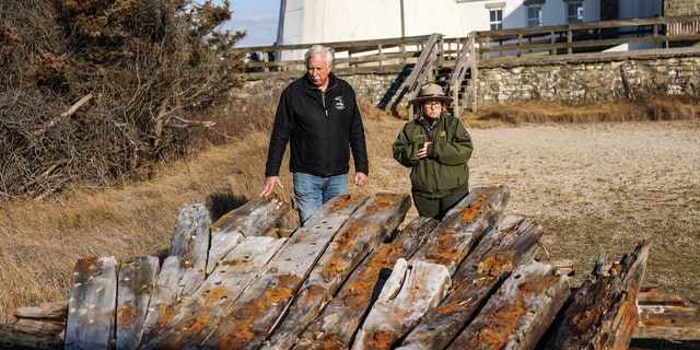 Tony Femminella, executive director of the Fire Island Lighthouse Preservation Society, and Betsy DeMaria, museum technician with Fire Island National Seashore, stand next to a section of the hull of a ship believed to be the SS Savannah which wrecked in 1821 off Fire Island on Jan. 27, 2023. The section now rests alongside the Fire Island lighthouse. 
