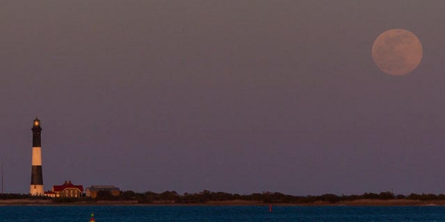 A full moon rises on the night of April 26, 2021, above the Great South Bay and the Fire Island Lighthouse. This full moon is a supermoon. 