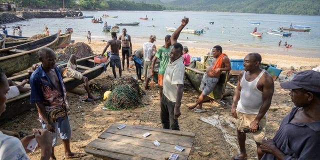 A group of men playing cards standing next to the fishing boats on the beach of Porto Alegre on Sao Tome Island in the Gulf of Guinea Feb 8, 2022.
