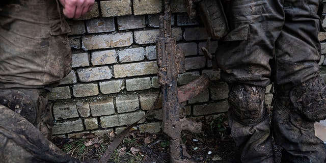A mud-stained gun is seen in front of Ukrainian servicemen which just come back from tranches of Bakhmut in Chasiv Yar, Ukraine, Wednesday, March 8, 2023. 