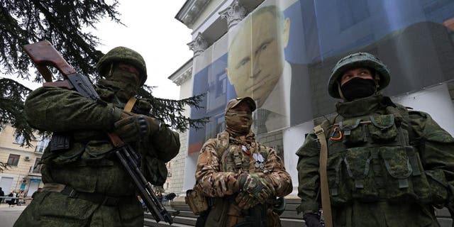 Participants dressed in military uniform stand in front of a banner with a portrait of Russian President Vladimir Putin during a patriotic flash mob marking the ninth anniversary of Russia's annexation of Crimea, in Yalta, Crimea March 17, 2023.