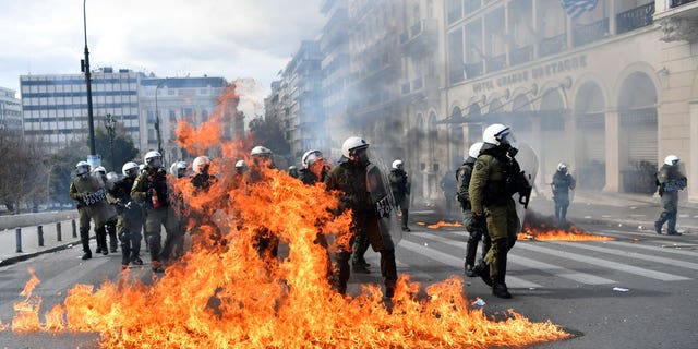 Riot polices take their positions next of flames of cocktail molotov after throwing of protestors during a 24-hours general strike in central Athens, on March 16, 2023.