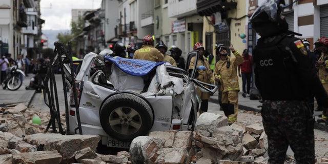 A police officer looks up next to a car crushed by debris after an earthquake shook Cuenca, Ecuador, Saturday, March 18, 2023.