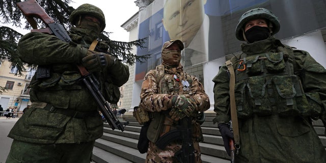 Participants dressed in military uniform stand in front of a banner with a portrait of Russian President Vladimir Putin during a patriotic flash mob marking the ninth anniversary of Russia's annexation of Crimea, in Yalta, Crimea March 17, 2023.