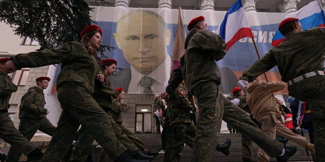 Participants march in front of a banner with a portrait of Russian President Vladimir Putin during a patriotic flash mob marking the ninth anniversary of Russia's annexation of Crimea, in Yalta, Crimea March 17, 2023.