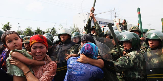 Chinese policemen push Uyghur women who are protesting the detention of their relatives on July 7, 2009, in Urumqi, the capital of Xinjiang province, China.